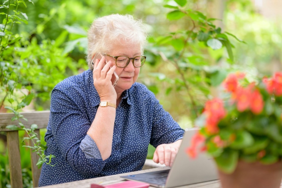 An older woman on the phone at her laptop in the garden